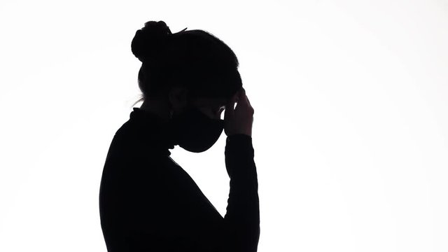 silhouette profile upset young woman in a protective mask praying on white isolated background, girl thinking about problem, health concept