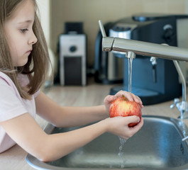 Cute young girl washing and sanitizing fresh fruit. Wash food. Child hands holding tasty apple...