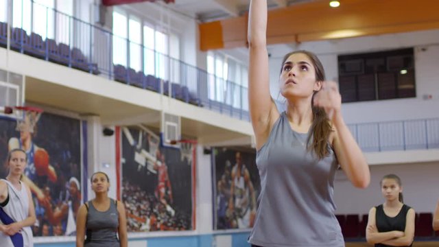 Young female athlete dribbling a basketball, throwing it and getting upset cause of missing the hoop while her teammates standing around on indoor court