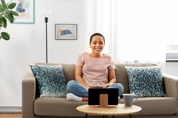 people, technology and leisure concept - happy young african american woman sitting on sofa with tablet pc computer and watching movie at home