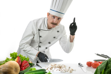 Chef cook stands with knife at the kitchen table with a mushroom and vegetables