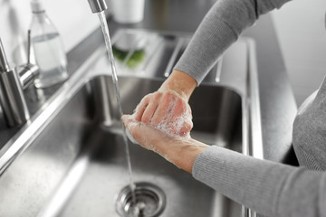 hygiene, health care and safety concept - close up of woman washing hands with liquid soap in kitchen at home