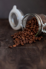Jar with coffee beans rashes on a wooden table. Coffee background close-up. Place for text, top view. The grain of an invigorating morning drink.