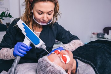 Cosmetologist in blue protective gloves makes the procedure of laser removal of permanent makeup of...