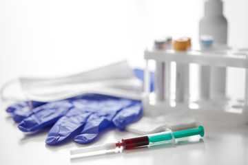 medicine and healthcare concept - close up of blood in syringe, mask, wound wipes and gloves at laboratory