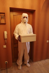 a man in a protective suit, mask and gloves with a box in his hands delivered the package box to the apartment to the door