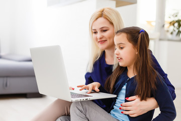 education, family and distant learning concept - mother and daughter with laptop computer doing homework together at home