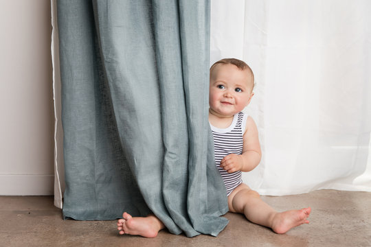 Cute baby sitting on floor by curtains at home