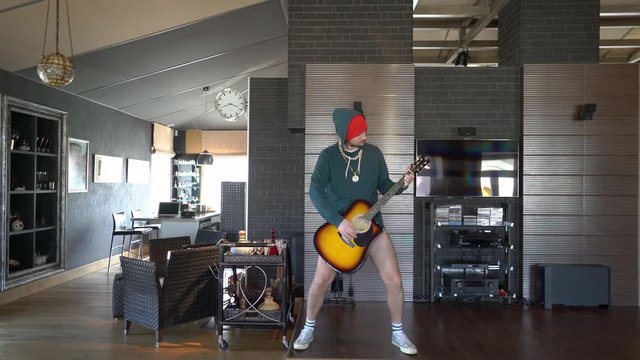 A young guy at home entertains himself on self-isolation with a guitar in his hand, he dances, he does not have pants and panties, a funny gay guy, a freak unusual sexy guy. Bored at home, covid-19.