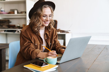 Image of cheerful woman working with laptop while sitting at table