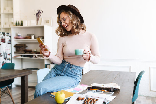 Image of woman using cellphone and drinking coffee while sitting