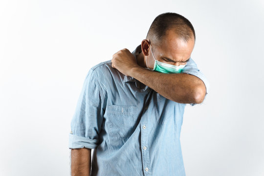 Man wearing face mask sneezing or coughing in his elbow to prevent spread the virus COVID-19 or Corona Virus on white background.