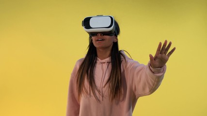 Multiracial girl using virtual reality glasses while standing against yellow background.