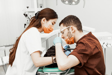 A young male dentist doctor treats a patient. Medical manipulations in dentistry, surgery. Professional uniform and equipment of a dentist. Healthcare Equipping a doctor’s workplace. Dentistry