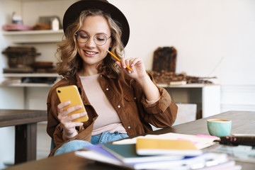 Image of woman using cellphone while studying with exercise books