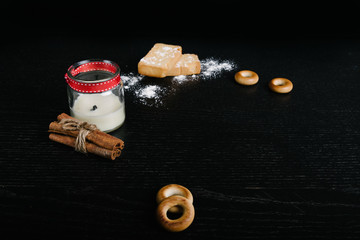 Simple set up for morniing coffee  . cup with saucer and few biscuits and bagels plus a bunch of cinnamon sticks and sugar powder for decoration. black background