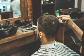 Haircut at the hairdresser. Barber cuts the hair on the client's head. The process of creating hairstyles for men. A man in a barbershop. The near plan. Equipment stylist. Selective focus