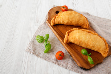 Homemade Deep Fried Italian Panzerotti Calzone on a rustic wooden board on a white wooden background, low angle view. Copy space.