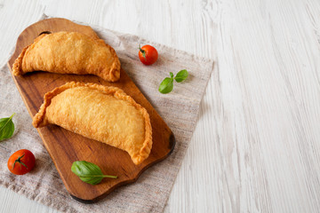 Homemade Deep Fried Italian Panzerotti Calzone on a rustic wooden board on a white wooden table, low angle view. Space for text.