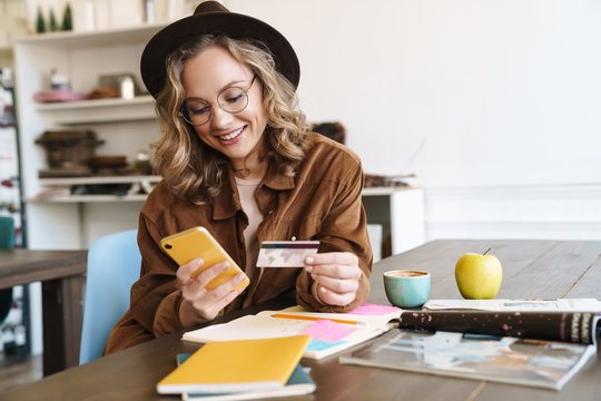 Image of smiling woman in hat using cellphone and holding credit card