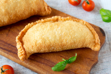 Homemade Deep Fried Italian Panzerotti Calzone on a rustic wooden board on a white wooden table, side view. Close-up.
