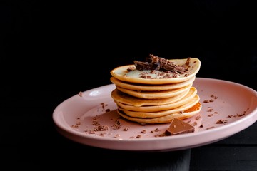 Close-up of delicious pancakes in a pink plate, with chocolate and condensed milk on a dark background.