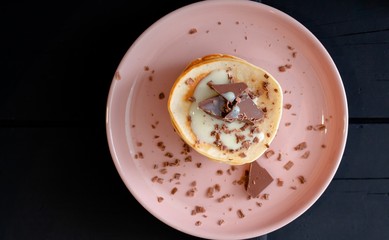Close-up of delicious pancakes in a pink plate, with chocolate and condensed milk on a dark background.