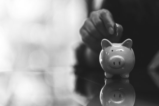 Black and white image of a woman putting coins into piggy bank for saving money concept