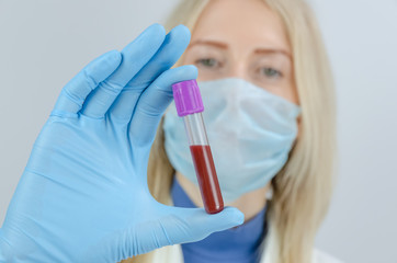 young blonde woman doctor holds a test tube with blood in her hand in blue gloves close-up. Concept of blood sampling, medical and chemical research