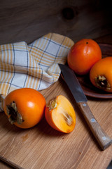 Whole ripe persimmon and sliced fruit on a wooden background..