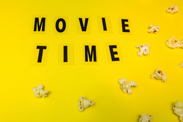 popcorn and text movie time on yellow paper background. Concept of cinema and entertainment. Flat lay
