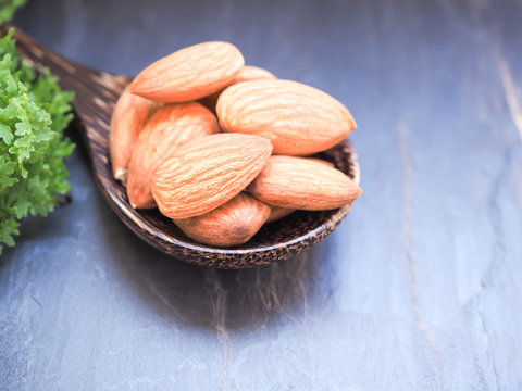 Group of almonds seeds in a wooden spoon on black stone background with space for text.