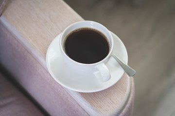 a Cup of coffee on a saucer with a spoon stands on the back of the sofa