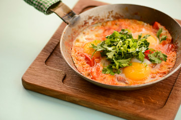 A freshly baked egg, tomato and green pepper frittata in a pan on wooden cutting board with blue mint background.