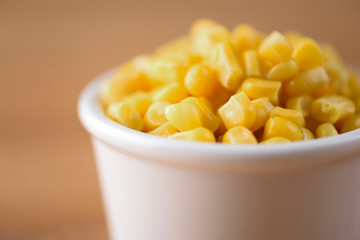 Sweet canned corn in a serving bowl over clurred wooden background.