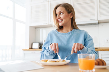 Image of cheerful young woman smiling while having breakfast
