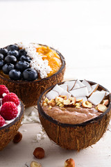 smoothie bowls with berries and fruit in coconut bowls on white background