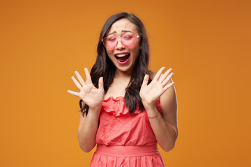 Screaming asian girl in pink glasses on empty orange background