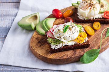 vegetarian toast with poached eggs, cottage cheese, avocado and vegetables on wooden Board