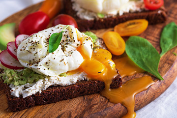 vegetarian toast with poached eggs with leaking yolk, cottage cheese, cherry tomatoes, radishes, spinach on wooden Board