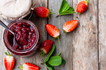 Strawberry jam in a glass jar with some fresh strawberry on wooden old rustic table. Homemade strawberry marmelade and fruits. Selective focus. Top view