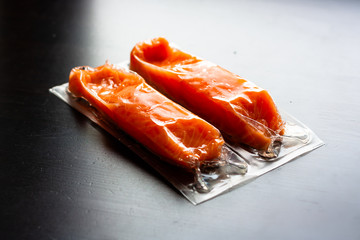 Red fish o salmon fillets in vacuum package on black background. Fresh fish and cooking ingredients. Omega-3. Close up. Selective focus. Copy space