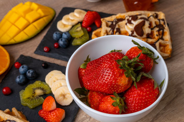 Tasty breakfast - close-up of strawberries with homemade waffles with fresh orange juice, fruit, milk and yogurt