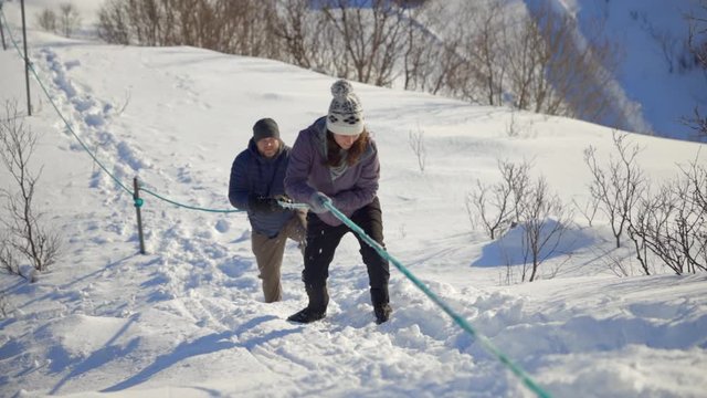A Man and A Woman Hiking up a Steep Snowy Mountainside Using a Rope, Slow Motion