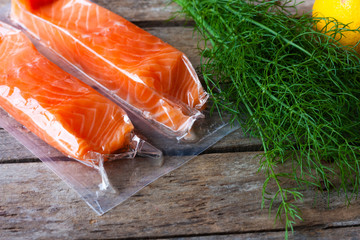 Red fish o salmon fillets in vacuum package on wooden background. Fresh fish, lemon and dill for...