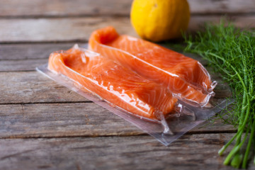 Red fish o salmon fillets in vacuum package on wooden background. Fresh fish, lemon and dill for cooking ingredients. Concept of healthy eating. Omega-3. Selective focus. Close up. Copy space
