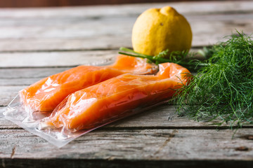 Red fish o salmon fillets in vacuum package on wooden background. Fresh fish, lemon and dill for cooking ingredients. Concept of healthy eating. Omega-3. Selective focus. Close up. Copy space