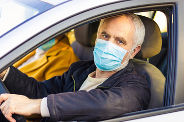 Senior man in a medical face mask driving a car. Coronavirus pandemic concept. Road trip, travel and old people concept - happy senior couple driving in car