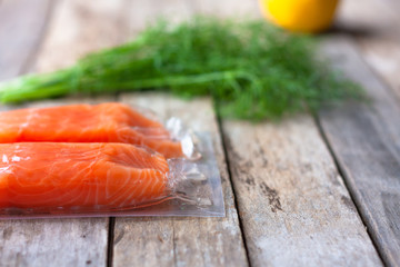 Red fish o salmon fillets in vacuum package on wooden background. Fresh fish, lemon and dill for cooking ingredients. Concept of healthy eating. Omega-3. Selective focus. Close up. Copy space