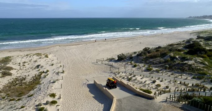 Surf life saver driving out to patrol the beautiful beach on a summer day. High angle drone tracking shot. Leighton Beach, Perth, Western Australia.